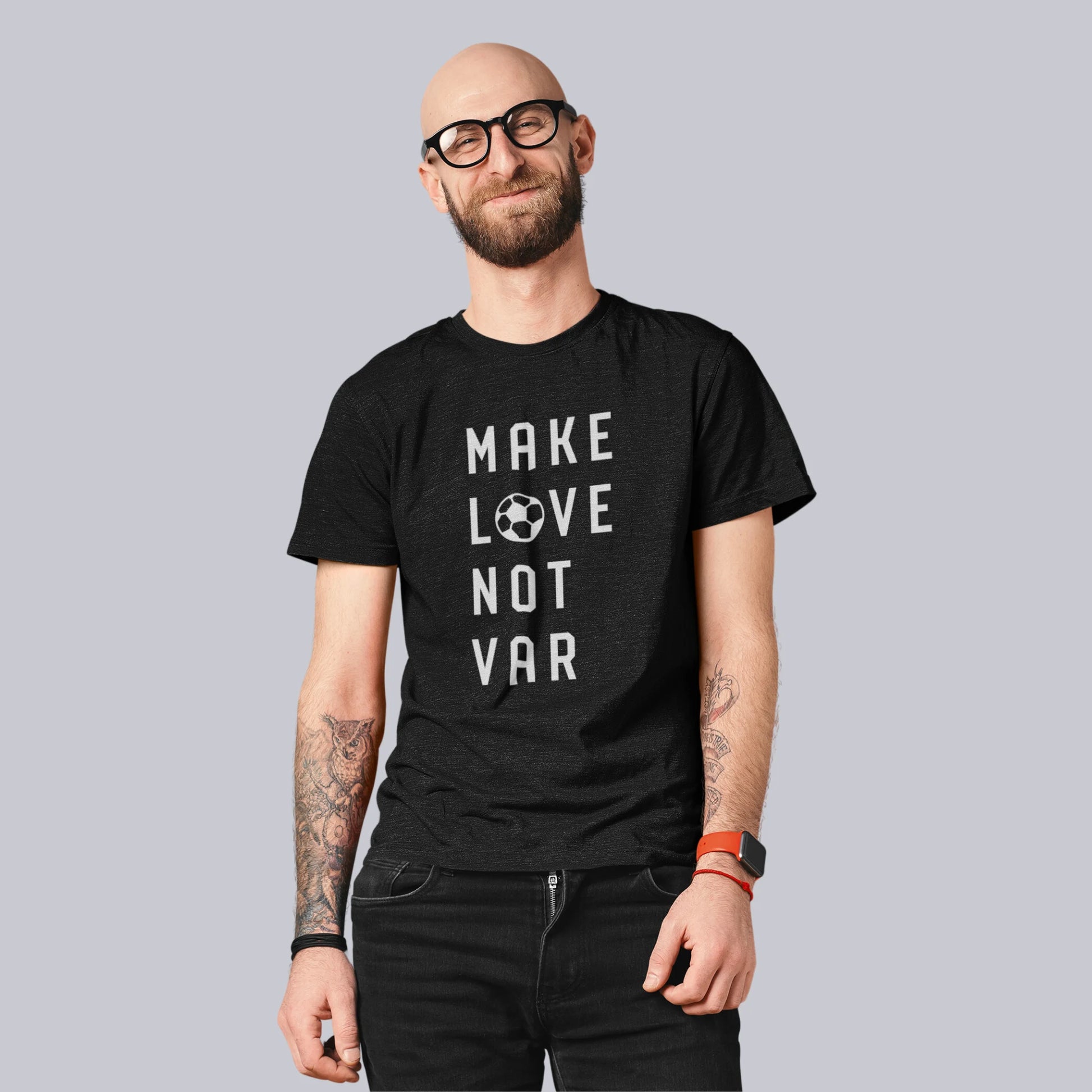 Smilende, skjeggete mann med briller og tatoveringer iført en svart T-skjorte med teksten "MAKE LOVE NOT VAR" i hvitt, hvor bokstaven "O" i "LOVE" er erstattet med en fotball.